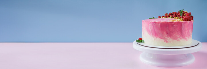 Celebratory cake with pink cream on a pink and blue background. Cake decor made from fresh raspberries, crushed pistachios and mint. Cake with raspberries. Great background with free space.