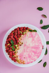 Celebratory cake with pink cream on a pink background. Cake decor made from fresh raspberries, crushed pistachios and mint. Green fresh mint leaves. Cake with raspberries. 