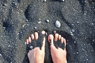 Bare feet in the sand at the Punalu'u black sand beach on the Big Island of Hawaii as viewed from...