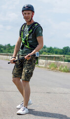 A  guy in the helmet and special equipment with an action camera is very happy and smiles after rope jumping from the bridge on the road