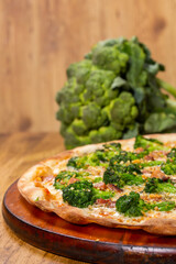 closeup of a broccoli pizza in front of a wooden background. Space for text