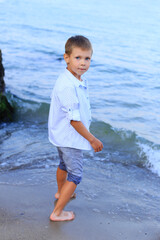 Beautiful boy stands on the seashore in summer