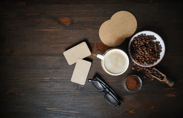 Fresh delicious coffee. Coffee cup, kraft business cards, roasted coffee beans, glasses and coffee ground on wooden background. Top view. Flat lay.