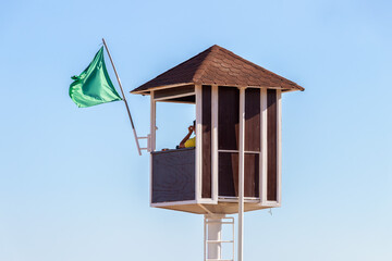A lifeguard sitting on surveillance tower. Red wooden lifeguard tower