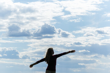 Fototapeta na wymiar The freedom to feel good and to travel is an adventure concept. Copy space of woman silhouette raising hands on blue sky and white cloud with background sunlight.