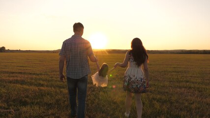 little daughter plays and jumps into field holding hands of mom and dad. healthy Happy family with child walks in park at sunset. baby and parent walk in sun. concept of happy family and childhood