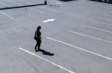 Woman walking on top of parkade roof with dramatic shadow from the bright sun