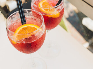 Closeup glasses of cocktail decorated with oranges on the table. Colorful pink soft drinks with ice and straws in a cafe.	