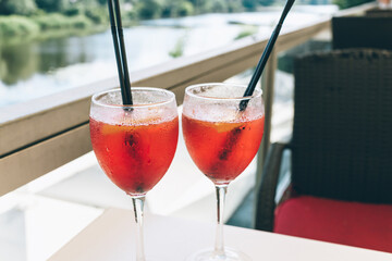 Closeup glasses of cocktail decorated with oranges on the table. Colorful pink soft drinks with ice and straws in a cafe. 