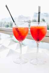 Closeup glasses of cocktail decorated with oranges on the table. Colorful pink soft drinks with ice and straws in a cafe. 