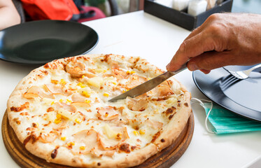 Mans hand cutting pizza on a plate with a knife. Still life, dinner in the cafe, pizzeria