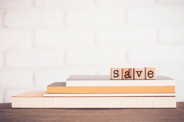 The word SAVE, alphabets on wooden rubber stamps on top of books with white bricks background, blank copy space, vintage minimal style. Concepts of budget management, bank, financial or protect.