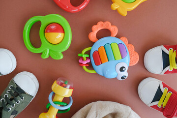 Baby accessories background. Plastic rattles and little baby shoes on brown background. Infancy concept.