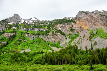 Fototapeta na wymiar Landscape view of mountain peak summit at Conundrum Creek Trail in Aspen, Colorado in 2019 summer with green lush plants trees on cloudy day and snow