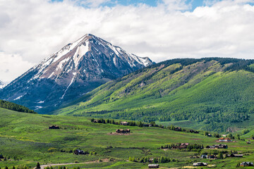 Fototapeta na wymiar Mount Crested Butte mountain peak and village in summer with hotel lodging houses on hills with green grass meadow color and snowcapped rocky mountains