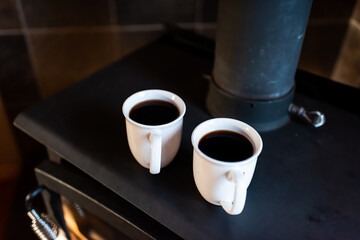 Closeup of two cups with black coffee or puerh tea on retro fireplace rustic vintage country home in morning