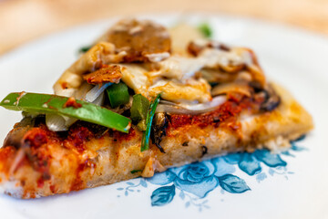 Homemade gluten free pizza slice cooked with tomato sauce, toppings of green bell peppers mushrooms and vegan sausage and melted cashew cheese on blue plate