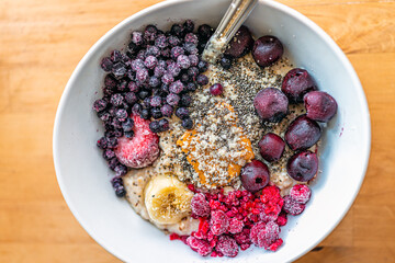 Flat top above closeup texture of oatmeal oat porridge bowl with peanut butter, frozen berries raspberries blueberries and cherries with banana and chia seeds