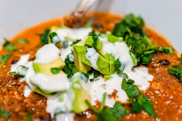 Macro closeup of bowl with fresh spicy chili pepper homemade soup with avocado and cashew sour cream topped with cilantro as vegan vegetarian dish
