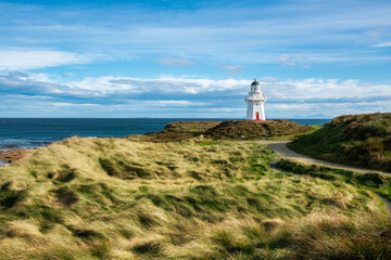 Fototapeta na wymiar The historic landmark lighthouse at Waipapa Point surrounded by grassy sand dunes on a sunny and cloudy day on the Dunedin coast