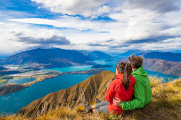 New Zealand hiking couple on mountain top Roys Peak relaxing sitting enjoying active outdoor...