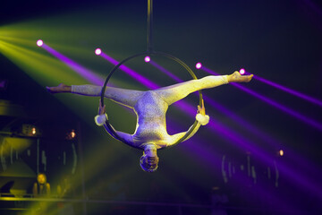 Flexible young woman make performance on aerial hoop, flexible back on aerial hoop, aerial circus show, yellow purple blue red light. Flexible woman gymnast upside down on hoop. Night club performance © Dima