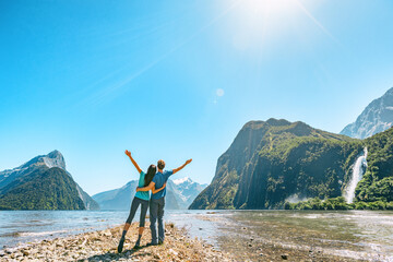 Outdoor couple happy with arms outstretched in Milford Sound New Zealand in nature enjoying active outdoor lifestyle hiking in Milford Sound, New Zealand by Mitre Peak in Fiordland. - obrazy, fototapety, plakaty