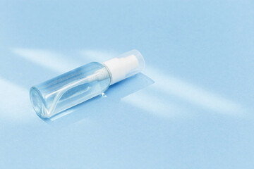 Naklejka premium Small bottle with transparent cosmetic product, gel or crem on blue colored background. Flack with moisturizer for self-care. Monochrome image.