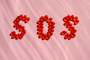 The letters SOS written in orange and red vitamins and pills on a dark pink striped background. Help.  Close-up.