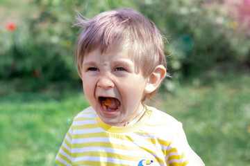 Portrait of a pretty boy with candy in his mouth on a summer day. A child of two years old opened...