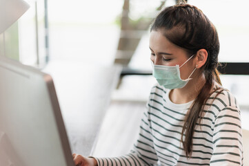 Beautiful asian woman wearing protection mask work from home in the morning. Young asian female working with computer stay at home.