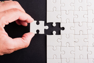 Top view flat lay of hand-holding last piece white paper jigsaw puzzle game last pieces put to...