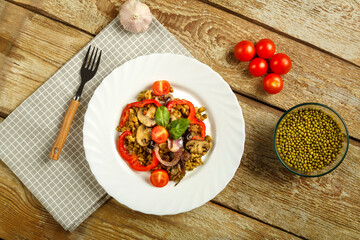 On a wooden table is a white dish of boiled mung bean with mushrooms and vegetables on a napkin and...