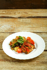 Baked chicken breast with tomatoes with a side dish of vegetables on a white plate. Copy space.