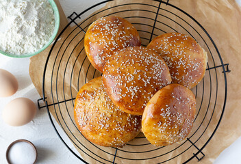 Burger buns covered with sesame seeds on baking grid and ingredients. Top view