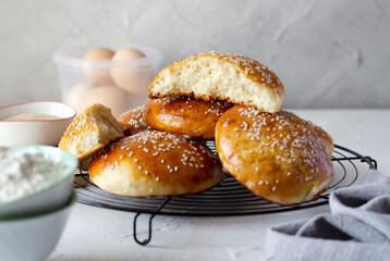 Buns covered with sesame seeds on baking grid and ingredients