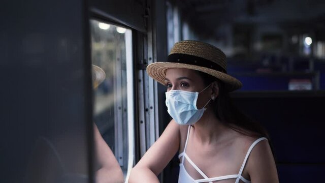 Young brunette woman traveling in Thailand on train during Coronavirus pandemic. 20s Hispanic girl in a protective mask wearing summer sleeveless clothes and backpack in Asia.