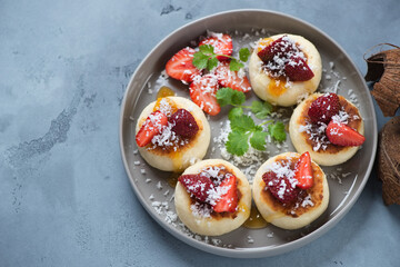 Curd pancakes or syrniki with fresh strawberries and coconut flakes, studio shot on a grey concrete background