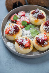 Closeup of cottage cheese pancakes with strawberries and coconut flakes on a round grey plate, selective focus, vertical shot