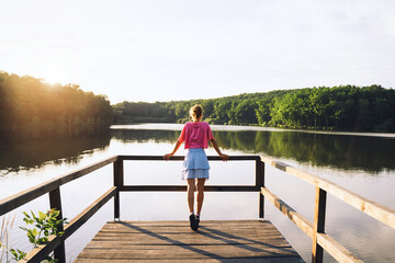 Fototapeta na wymiar Woman on wooden bridge near lake on green nature background.