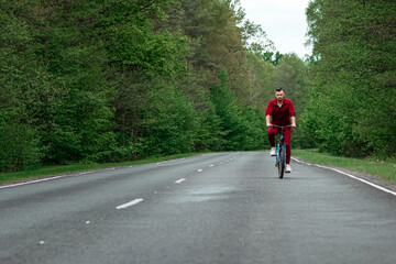 Obraz premium A man in a tracksuit on a bicycle rides on a road in the forest. The concept of a healthy lifestyle, cardio training. Copyspace.