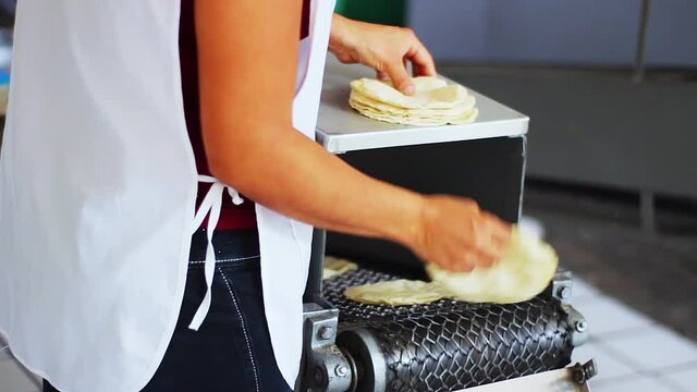 Woman stacking fresh corn tortillas from tortilla making machine traditional mexican