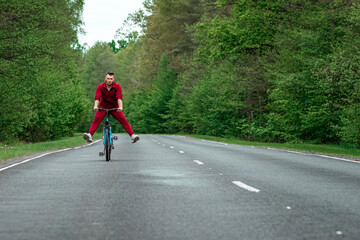 Happy male riding bike with legs up. The road in the forest. The concept of a healthy lifestyle, cardio training. Copyspace.