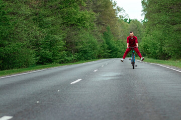 Happy male riding bike with legs up. The road in the forest. The concept of a healthy lifestyle, cardio training. Copyspace.