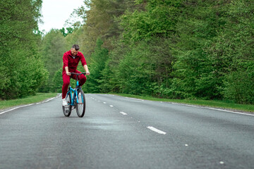 Naklejka premium A man in a tracksuit on a bicycle rides on a road in the forest. The concept of a healthy lifestyle, cardio training. Copyspace.