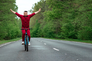 Fototapeta premium A man in a tracksuit rides a bicycle without hands on the road in the forest. The concept of a healthy lifestyle, cardio training. Copyspace.