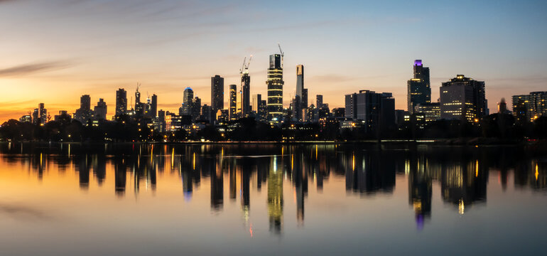 The reflections of the melbourne city skyline at dusk in the still water of albert park lake