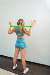 rear view. girl with tattoos are engaged fitness with rubber bands in home. 