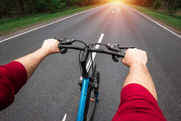 Fototapeta na wymiar Male hands on the handlebars of a bicycle riding on a road in the forest. The concept of a healthy lifestyle, cardio training. Copyspace.