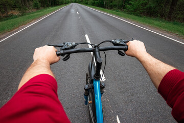 Fototapeta na wymiar Male hands on the handlebars of a bicycle riding on a road in the forest. The concept of a healthy lifestyle, cardio training. Copyspace.